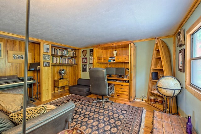 home office with light wood-type flooring, crown molding, a textured ceiling, and wooden walls