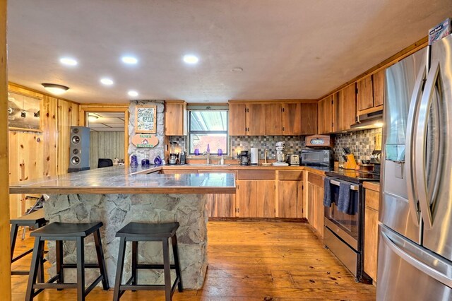 kitchen with light hardwood / wood-style floors, sink, a breakfast bar area, decorative backsplash, and appliances with stainless steel finishes