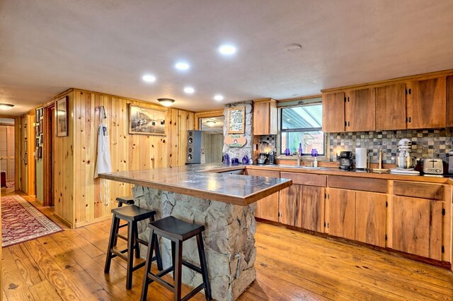 kitchen featuring a kitchen breakfast bar, light wood-type flooring, kitchen peninsula, and tasteful backsplash