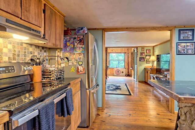 kitchen with appliances with stainless steel finishes, light wood-type flooring, ornamental molding, and decorative backsplash