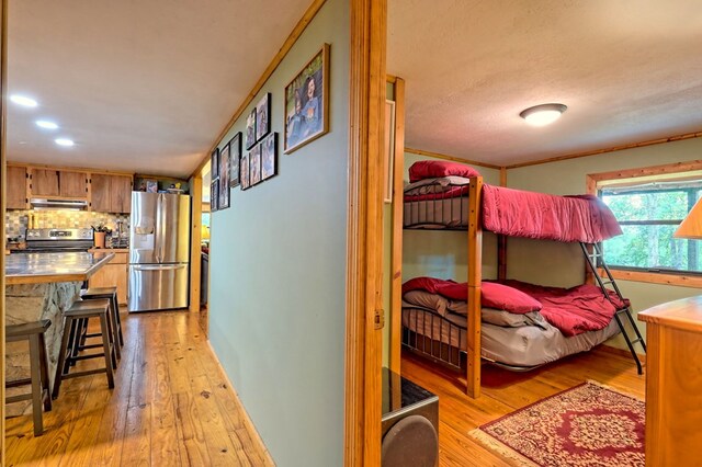 bedroom with light hardwood / wood-style floors, crown molding, and stainless steel fridge