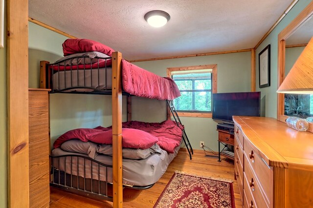 bedroom featuring light hardwood / wood-style flooring, a textured ceiling, and ornamental molding