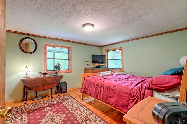 bedroom with a textured ceiling, light wood-type flooring, and crown molding