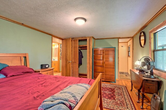 bedroom featuring a textured ceiling, light hardwood / wood-style flooring, ensuite bath, and ornamental molding