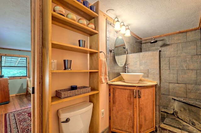 bathroom with vanity, toilet, a textured ceiling, a tile shower, and hardwood / wood-style floors