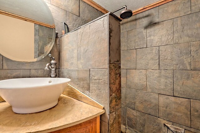 bathroom with a textured ceiling, a tile shower, and vanity