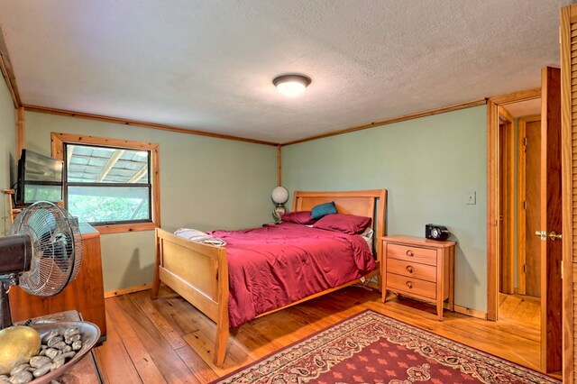 bedroom featuring ornamental molding, light wood-type flooring, and a textured ceiling