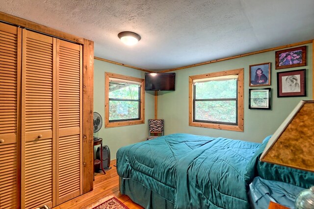 bedroom featuring light hardwood / wood-style flooring, a closet, multiple windows, and a textured ceiling