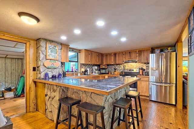 kitchen with kitchen peninsula, a kitchen bar, light hardwood / wood-style flooring, and stainless steel appliances