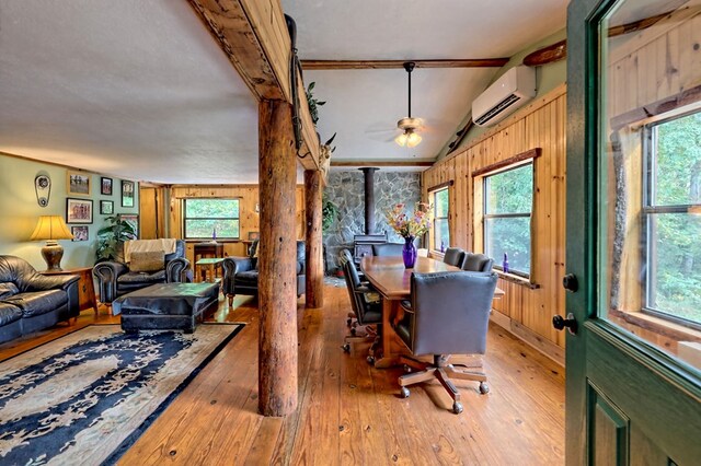 dining space with wood-type flooring, an AC wall unit, a wood stove, and plenty of natural light