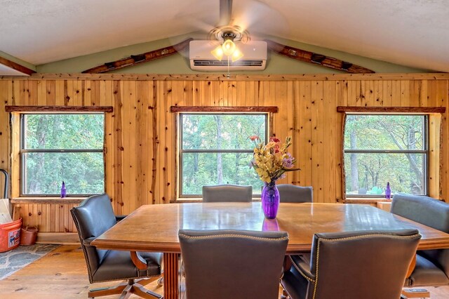 dining area with vaulted ceiling, wood-type flooring, ceiling fan, wooden walls, and a wall mounted air conditioner