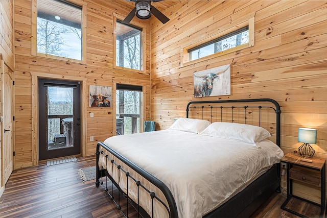 bedroom with a towering ceiling, access to outside, dark hardwood / wood-style floors, and wood walls