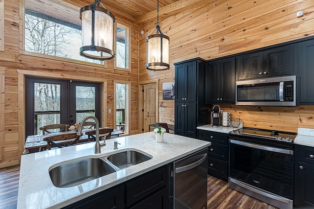 kitchen with light stone counters, hanging light fixtures, stainless steel appliances, and wood walls