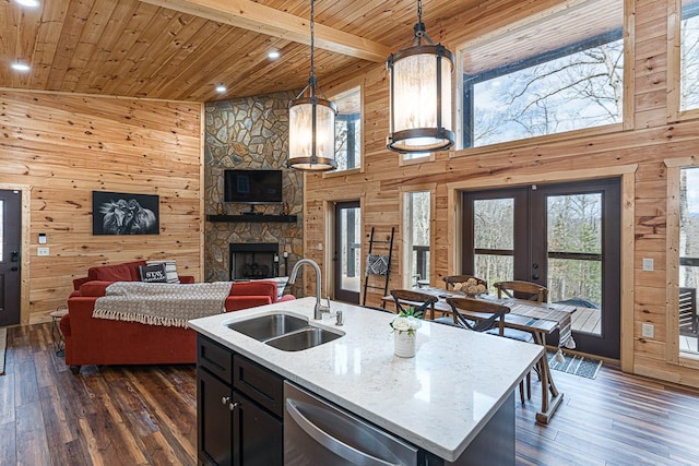 kitchen featuring sink, wood walls, decorative light fixtures, light stone countertops, and a kitchen island with sink