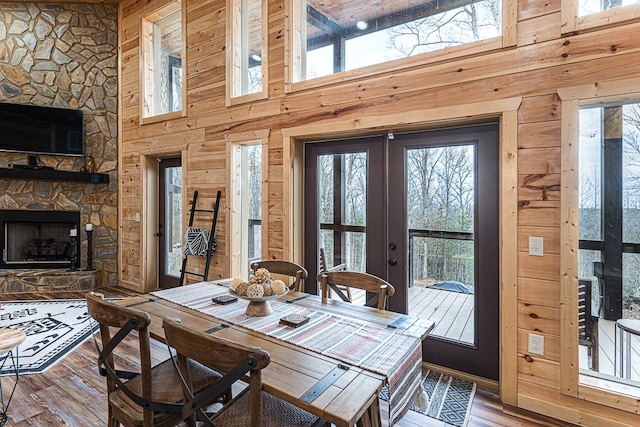 dining room featuring wooden walls, a fireplace, wood-type flooring, a high ceiling, and french doors