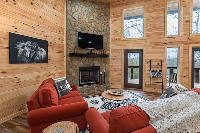 living room with plenty of natural light, wood-type flooring, a stone fireplace, and wood walls