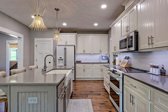 kitchen featuring a breakfast bar, a kitchen island with sink, dark wood-type flooring, hanging light fixtures, and stainless steel appliances