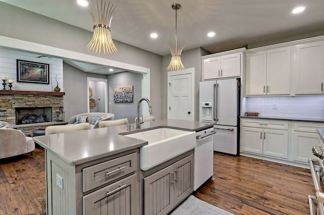 kitchen featuring white appliances, dark wood-type flooring, sink, a fireplace, and white cabinetry