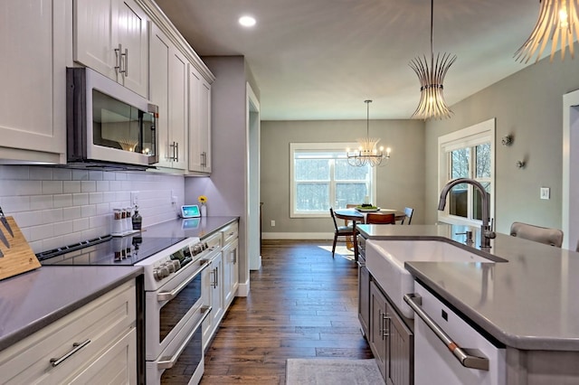 kitchen with sink, stainless steel appliances, dark hardwood / wood-style floors, a notable chandelier, and decorative light fixtures