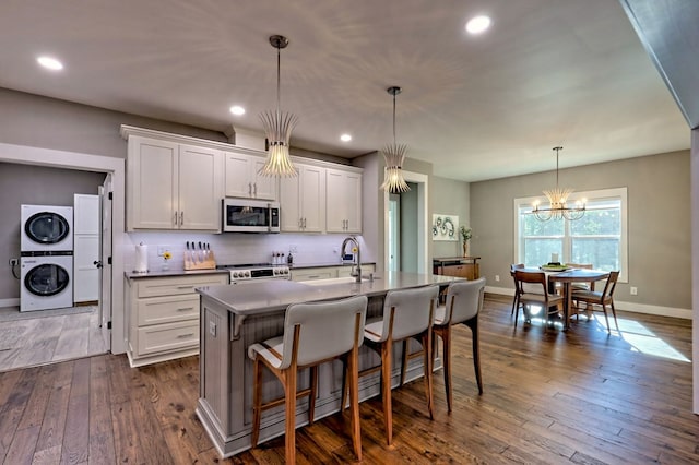 kitchen with white cabinets, appliances with stainless steel finishes, stacked washing maching and dryer, and an island with sink