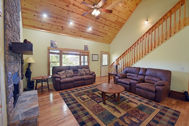 living room featuring wood ceiling, ceiling fan, high vaulted ceiling, light hardwood / wood-style flooring, and a stone fireplace