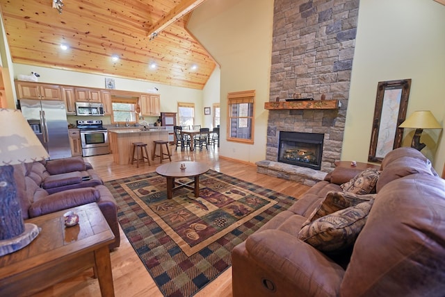 living room with wooden ceiling, high vaulted ceiling, a stone fireplace, light hardwood / wood-style flooring, and beamed ceiling