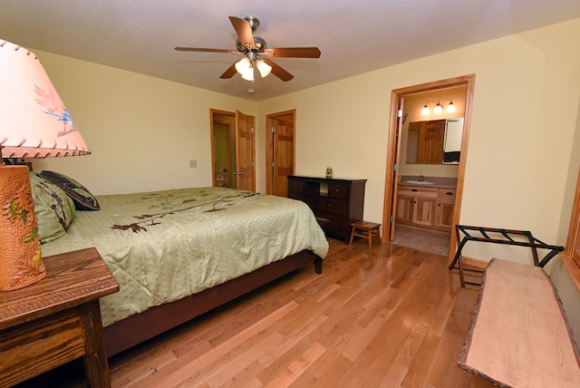 bedroom featuring ceiling fan, sink, ensuite bathroom, a textured ceiling, and light wood-type flooring