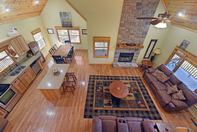 living room featuring ceiling fan, sink, a stone fireplace, high vaulted ceiling, and light wood-type flooring