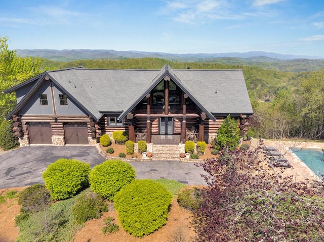 log cabin with a garage, log exterior, aphalt driveway, a mountain view, and a porch