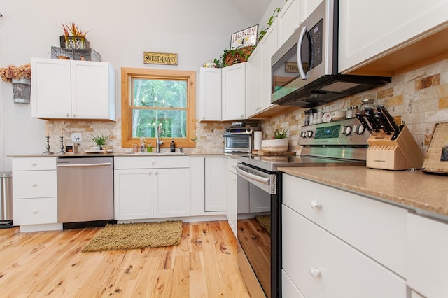 kitchen with backsplash, stainless steel appliances, white cabinetry, and light wood-type flooring