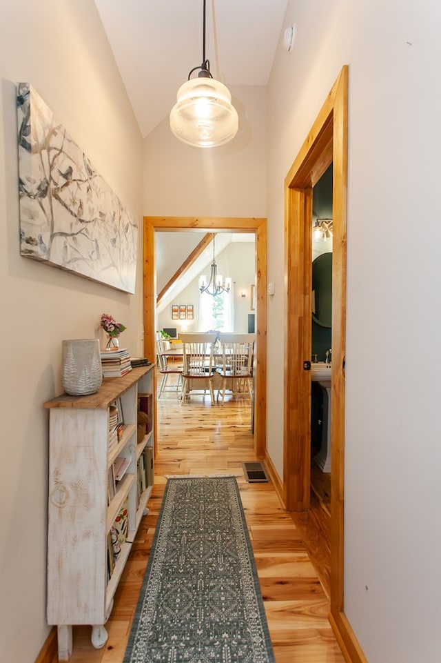 corridor featuring light wood-type flooring, vaulted ceiling, and a chandelier