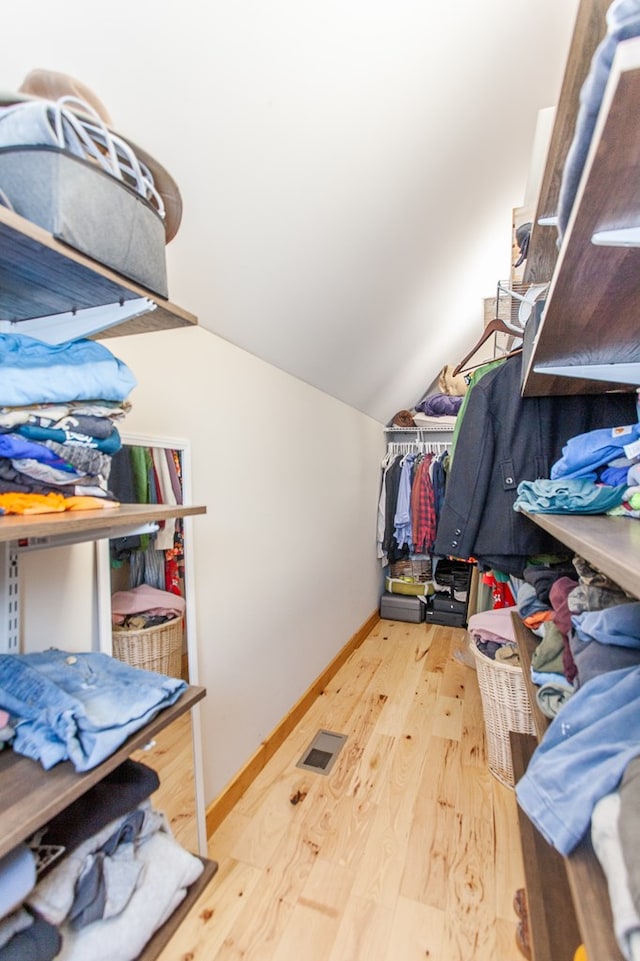 walk in closet with light hardwood / wood-style floors and vaulted ceiling