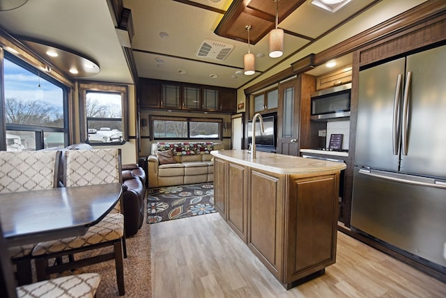 kitchen with appliances with stainless steel finishes, pendant lighting, an island with sink, dark brown cabinetry, and light hardwood / wood-style flooring