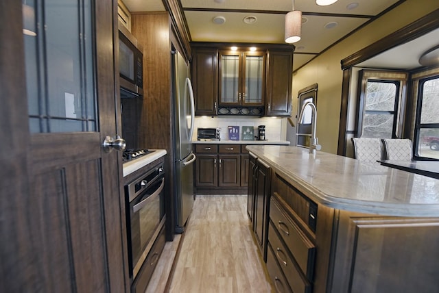 kitchen with appliances with stainless steel finishes, pendant lighting, decorative backsplash, a center island, and light hardwood / wood-style flooring