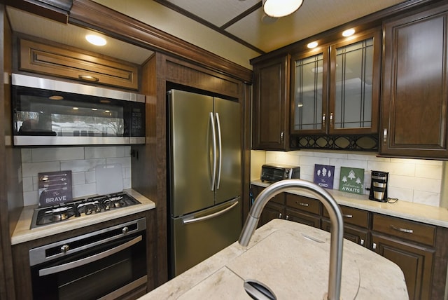 kitchen featuring tasteful backsplash, appliances with stainless steel finishes, built in desk, and dark brown cabinetry