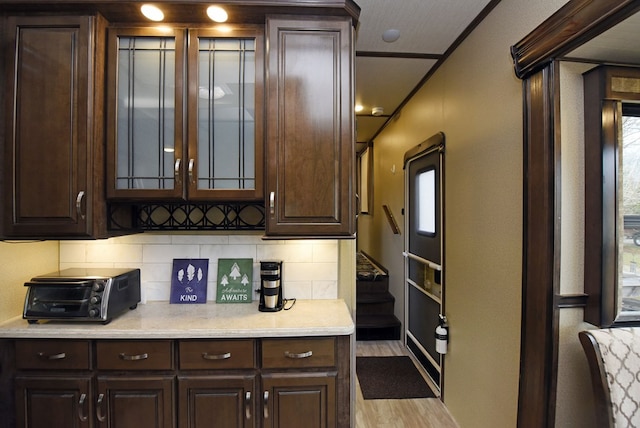 bar featuring dark brown cabinetry, backsplash, and light hardwood / wood-style floors