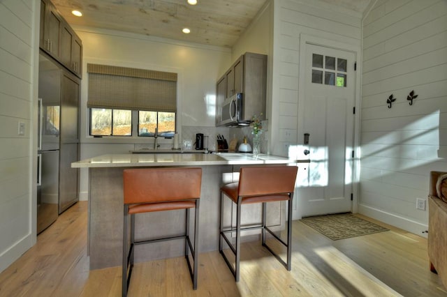 kitchen with a breakfast bar area, light wood-style flooring, built in fridge, stainless steel microwave, and tasteful backsplash