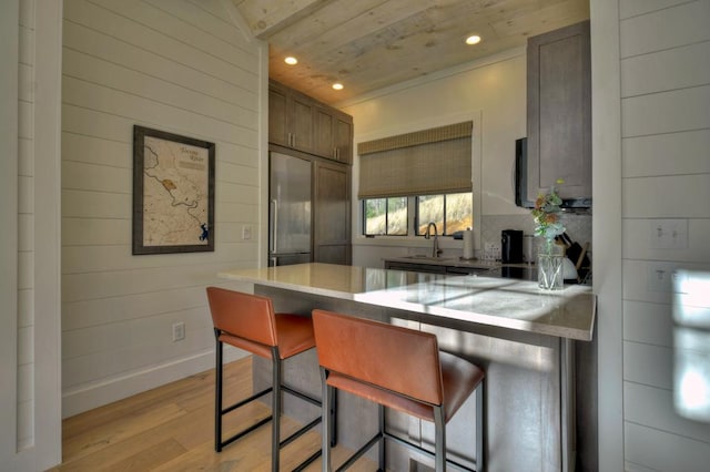 kitchen featuring built in refrigerator, a sink, light wood-style floors, a peninsula, and a breakfast bar area