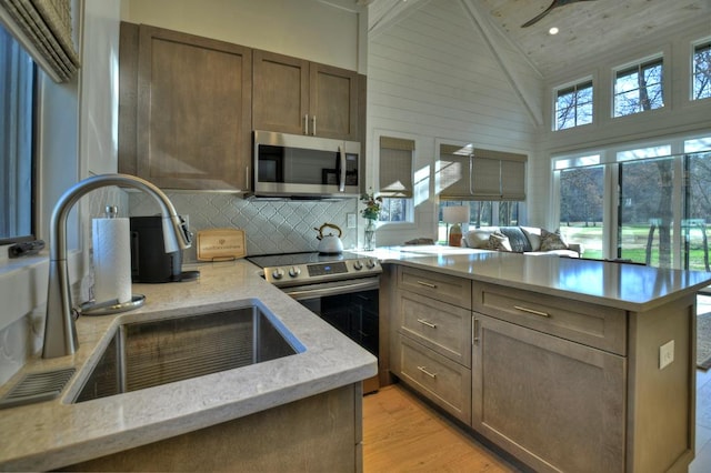 kitchen with decorative backsplash, a peninsula, light wood-style floors, stainless steel appliances, and a sink