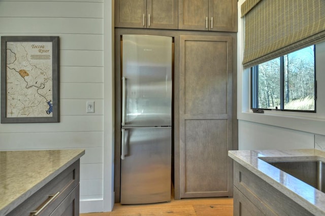 kitchen with light stone counters, stainless steel fridge, light wood-type flooring, and wood walls