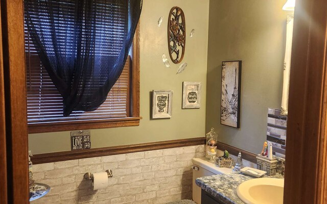 half bathroom featuring vanity, a wainscoted wall, and toilet