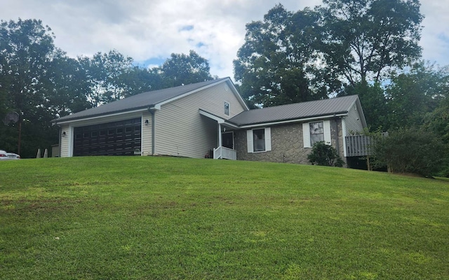 view of front of property featuring an attached garage, metal roof, a front yard, and stone siding