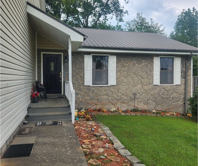 doorway to property featuring stone siding, a yard, and metal roof