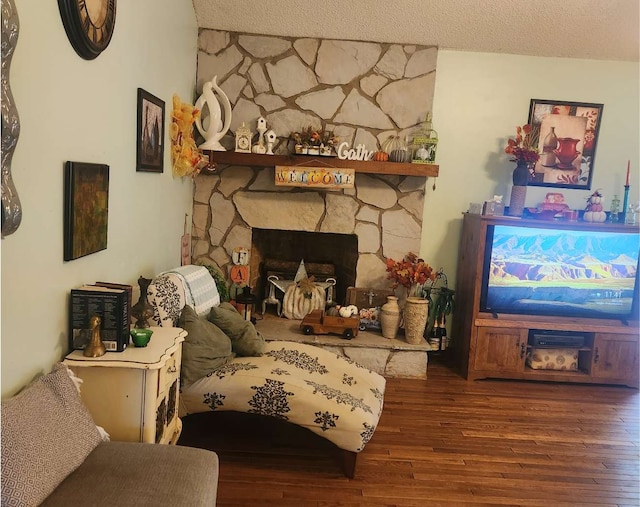 living room featuring hardwood / wood-style floors, a textured ceiling, and a stone fireplace