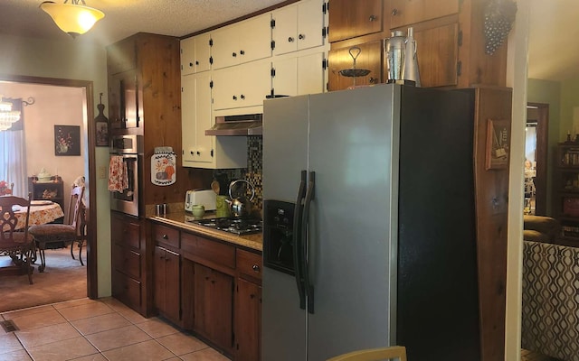 kitchen featuring stainless steel appliances, under cabinet range hood, light tile patterned floors, white cabinets, and light colored carpet