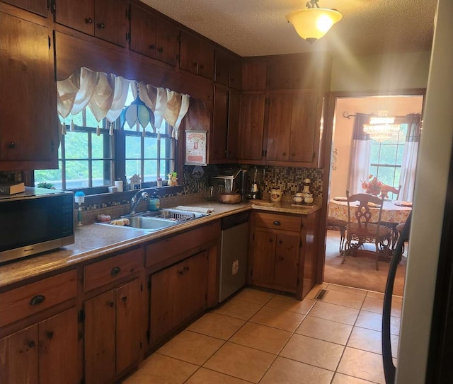kitchen featuring appliances with stainless steel finishes, a sink, healthy amount of natural light, a textured ceiling, and light tile patterned floors