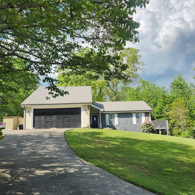 view of front of house with stone siding, driveway, an attached garage, a front lawn, and metal roof