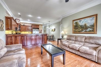 living room featuring ceiling fan, crown molding, and light hardwood / wood-style flooring