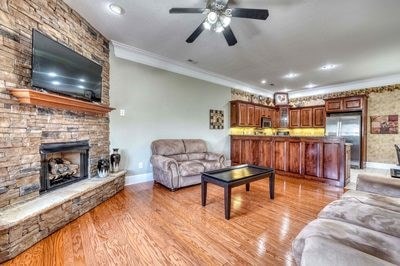 living room featuring light hardwood / wood-style floors, a stone fireplace, ceiling fan, and ornamental molding