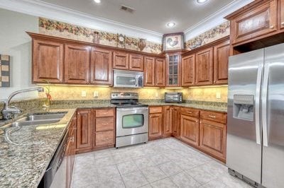 kitchen featuring light stone counters, sink, stainless steel appliances, and ornamental molding